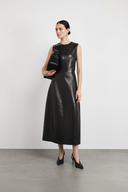 Woman wearing a black leather dress holding a matching handbag against a white background